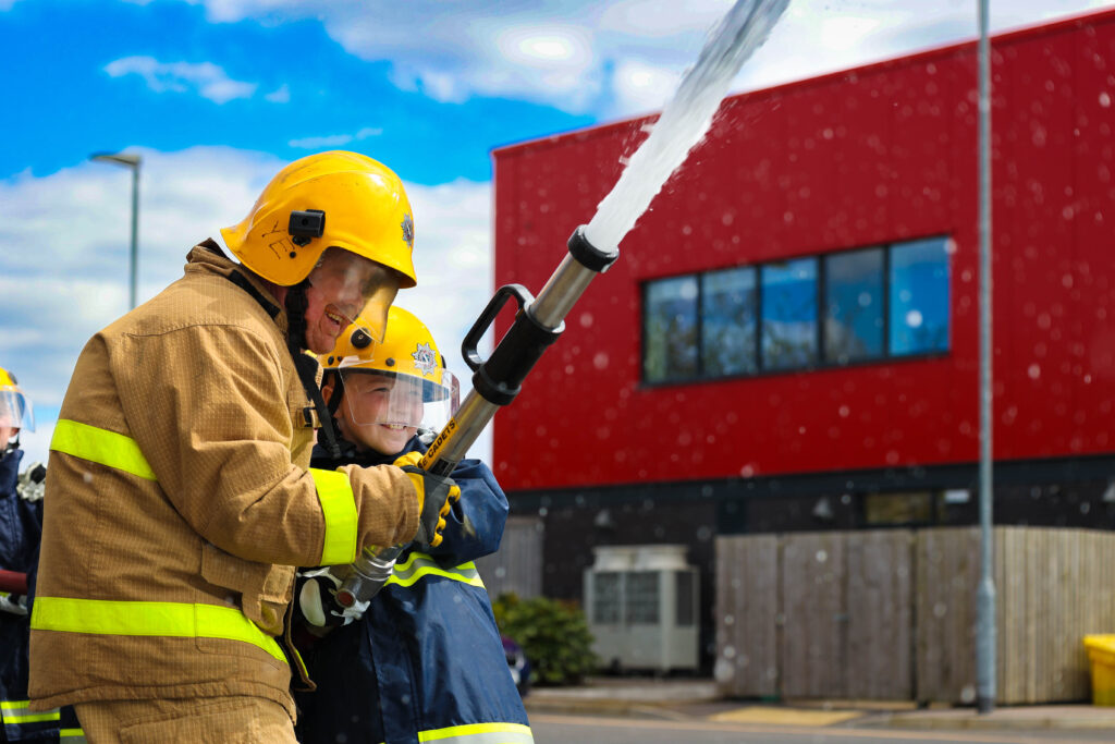 young boy with fire officer holding the water hose