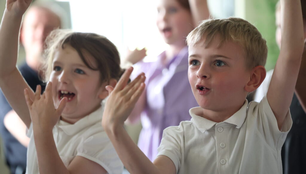 Primary school pupils from Dovecot Primary School with their hands in air